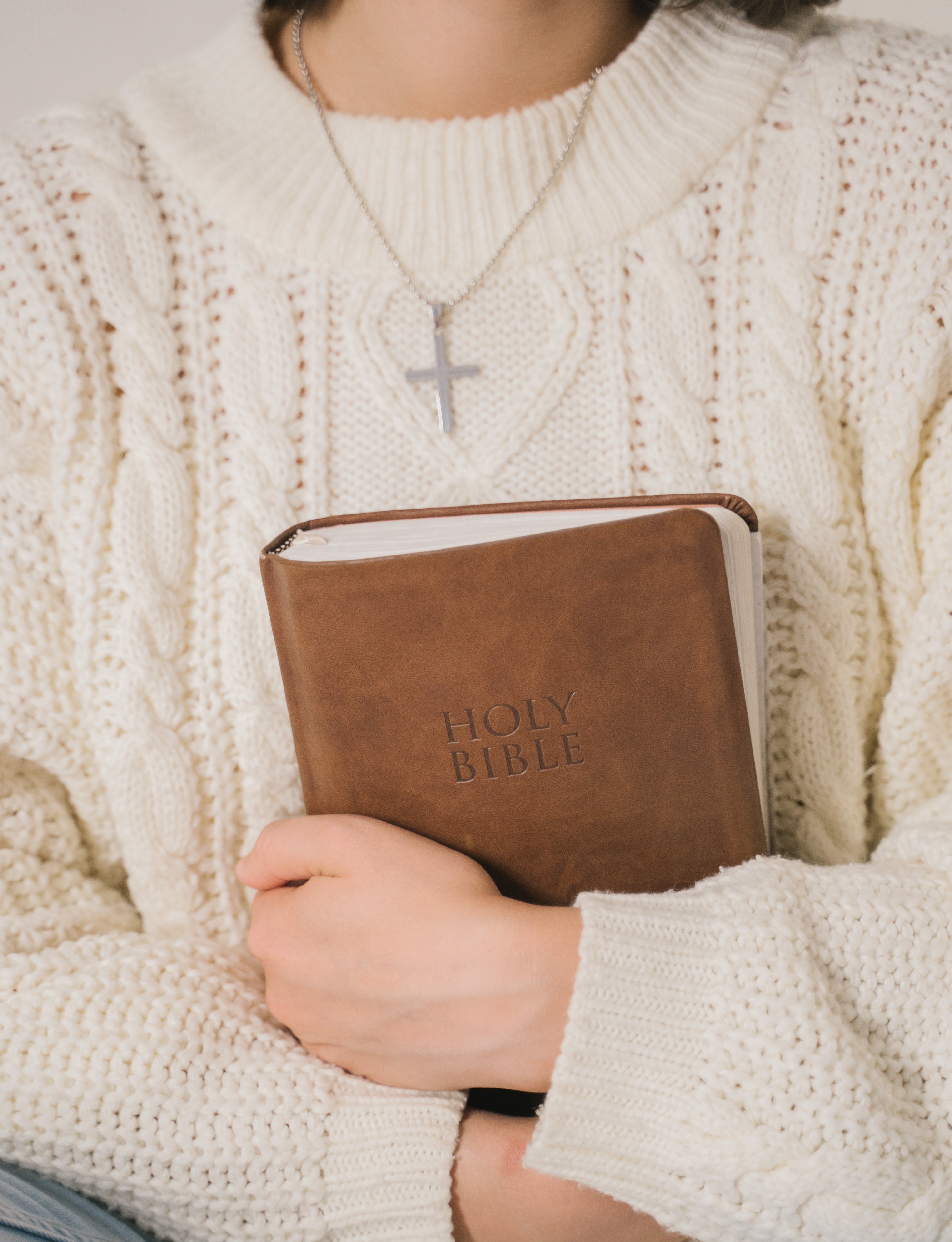 Nainen puristaa sylissään raamattua. Hänellä on valkoinen villapaita ja ristikaulassa.